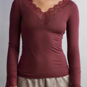 Intimissmi spets topp - Elegant vinröd topp med långa ärmar och v-ringad spetsdetalj vid halsen. Tillverkad i ett mjukt material som ger en bekväm passform. Perfekt för en stilren look. Köpt på intimissmi o säljer pga att den sitter lite för stort på mig