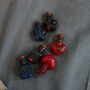 Färgglada små flaskor i olika former - Säljer ett set med små dekorativa flaskor i olika former och färger. Setet innehåller stjärnformade flaskor i blått, vitt, svart och rött, fyrkantiga flaskor i vitt, blått, svart och rött, samt hjärtformade flaskor i rött. Perfekta som dekoration eller för små presenter.