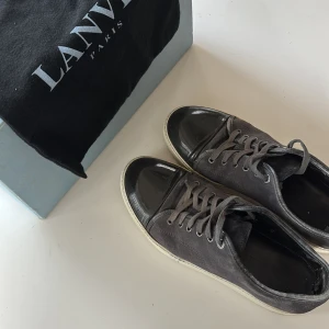 Gråa Lanvins - Snygga grå sneakers från Lanvin med svart glansig tå och snörning. Perfekt för våren och sommaren. Försiktigt använda, hälen inuti är lite sliten men märks inte när man har på dem. Skriv vid frågor! Size 8 uk, 43-44 EU.
