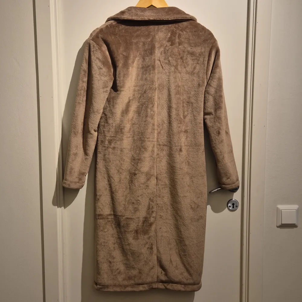 Mysig beige teddyjacka med lång längd och klassisk krage. Perfekt för kyliga dagar när du vill hålla dig varm och stilren. Jackan har långa ärmar och en mjuk, fluffig yta som ger en skön känsla. En knapp för att stänga jackan och den har inga fickor.. Takit.