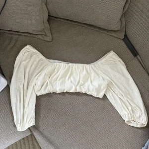 Vit offshoulder blus - Säljer en söt vit offshoulder blus med puffiga ärmar. Perfekt för en somrig look. Blusen har en elastisk kant vid axlarna för en bekväm passform. Är storlek L men väldigt stretchig så passar mig som har S/M i vanliga fall också 