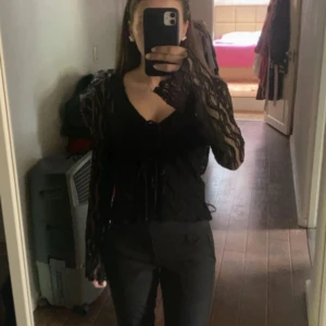 Svart spetsblus - Säljer en elegant svart spetsblus med långa ärmar och knytning framtill. Perfekt för en stilren look. ALDRIG ANVÄND!