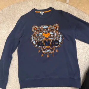 Mörkblå sweatshirt med tigerbroderi från Kenzo - Säljer en mörkblå sweatshirt från Kenzo med ett stort, färgglatt tigerbroderi på framsidan. Tröjan har långa ärmar och en rund halsringning. Perfekt för en cool och avslappnad stil. 🐯