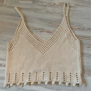 Beige stickad linnetopp - Säljer en beige stickad linnetopp med smala axelband och v-ringning. Toppen har ett dekorativt hålmönster och en unik kantdetalj längst ner. Perfekt för varma sommardagar. Storlek S, från chiquelle men bortklippt lapp 