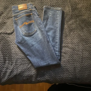 Blå jeans från Nudie Jeans - Snygga blå jeans från Nudie Jeans med klassisk femficksdesign och kontrastsömmar. De har en knappgylf och är tillverkade i ett slitstarkt denimtyg. Perfekta för en avslappnad stil. Riktigt feta jeans i helt perfekt skick, så gott som nya🤩🤩 Vid intresse/ mer bilder är det bara att kontakta!! 🚨Snabb affär=lägre pris🚨