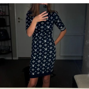 Mörkblå klänning med mönster - Snygg mörkblå klänning med ett vitt geometriskt mönster. Klänningen har trekvartsärmar och en figurnära passform som framhäver silhuetten. Perfekt för en stilren look.