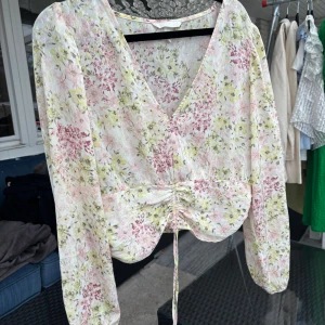 Blommig blus med knytning - Säljer en söt blommig blus med v-ringning och knytning framtill. Blusen har långa ärmar och ett romantiskt mönster i rosa och gröna toner. Perfekt för vår och sommar!🌸💕💕🌸