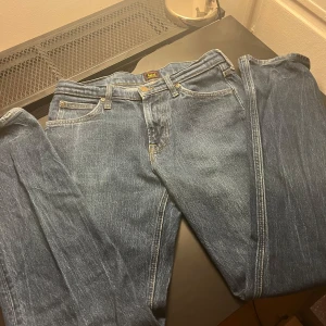 Blå jeans från Lee - Snygga blå jeans från Lee med klassisk femficksdesign och guldfärgade knappar. De har en rak passform och är perfekta för en avslappnad stil. Tillverkade i slitstarkt denim.
