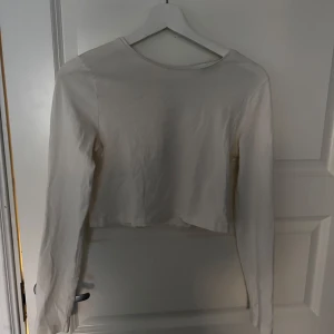 Vit croppad topp från Bik Bok - Säljer en stilren vit croppad topp från Bik Bok. Toppen har långa ärmar och en dragkedja framtill som ger en cool detalj. Perfekt för att matcha med höga jeans eller kjol. Passar bra till både vardag och speciella tillfällen.