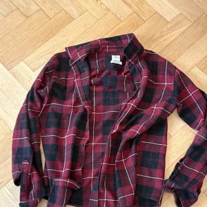  skjorta i röd och svart - Snygg rutig skjorta från H&M i röd och svart med knappar framtill. Perfekt för en avslappnad stil. Skjortan har långa ärmar och en klassisk krage.