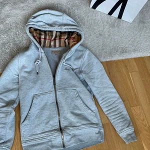 Grå huvtröja från Burberry - Säljer denna stil rena zip hoddien från Burberry köpt på nk herr trender. Säljes p.ga använder den sällan. Strlk S men passar även xs. Obs kvitto saknas. Har du några funderingar? Tveka inte på att höra av dig. Nypris ca 3,500-4000kr.