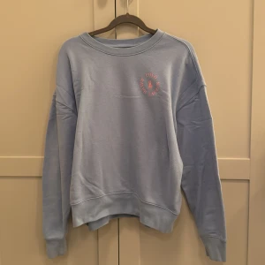 Blå sweatshirt från Polo Ralph Lauren - Säljer en snygg ljusblå sweatshirt från Polo Ralph Lauren med deras  logga i rosa på bröstet. Tröjan har långa ärmar och en klassisk rund halsringning. Perfekt för en avslappnad stil. 🩵