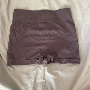 Mörklila seamless träningstights shorts - Mörklila seamless shorts med hög midja och ribbad linning. Tight passform och scrunch-detalj bak för extra shaping. Perfekta för gymmet eller yoga. Mjukt och stretchigt material som sitter skönt på kroppen.