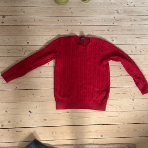 Röd kabelstickad tröja Polo Ralph Lauren - Säljer en röd kabelstickad tröja från Polo Ralph Lauren. Tröjan har lång ärm, rund halsringning och klassisk broderad logga på bröstet. Tillverkad i mjuk bomull och passar perfekt för dig som gillar en tidlös och snygg stil.