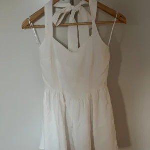 Vit kortklänning från Nalina med rosett - Superfin vit kortklänning oanvänd från Nalina med breda axelband och stor rosett i nacken. Klänningen har subtilt blommönster i tyget, v-ringning och dragkedja bak. Perfekt för sommarens alla tillfällen när du vill känna dig extra söt. skriv ifall ni vill se bilder på:)  Nypris: 1865kr