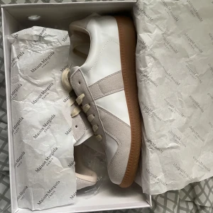 Maison Margiela sneakers - Hej! Säljer ett par Maison Margiela sneakers i vit och beige färg. Skorna är äkta och kommer med låda och påse. De är i storlek 42 och är i nyskick. Testade skorna och passade väldigt bra men har tyvärr inga kläder som passar med dem :) De är perfekta för dig som tycker om Maison och har en fet sommarfit till dem. Priset är 2400kr.
