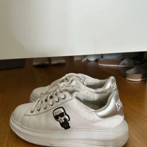 Vita sneakers från Karl Lagerfeld - Stilrena vita sneakers från Karl Lagerfeld med silverdetaljer på hälen och en cool Karl Lagerfeld-figur på sidan. Skorna har snörning och en chunky platt sula. Perfekta för dig som gillar en trendig och sportig look.