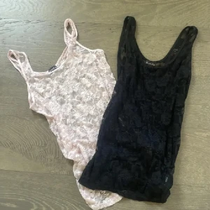 2 spetslinnen från Dressed Up - Två linnen i spets från Dressed Up, ett i svart och ett i ljusrosa. Båda är ärmlösa med smala axelband och har ett blommigt spetsmönster över hela tyget. Perfekta att styla lager på lager eller som statement-plagg.