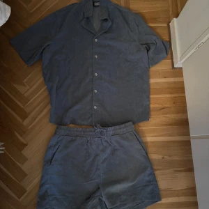 Blått set med mjukis och skjorta i manchester - Snyggt blått set i manchester med korta ärmar och knappar framtill. Skjortan har en avslappnad passform och är perfekt för varma dagar. Matcha med shorts för en cool sommarlook.
