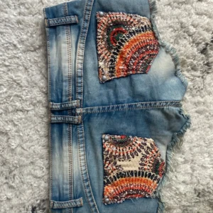 Blå lowwaist mini jeansshorts med paljettfickor - Snygga low waist mini jeansshorts i strl 36, midja:36cm. Kommer fler unika jeansshorts/kjolar så följ!!