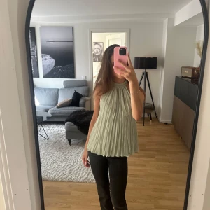 Ljusgrön plisserad ärmlös blus - Säljer en flowy ljusgrön blus med plisserat tyg och hög hals. Toppen är ärmlös och har en lätt glansig finish som ger en lyxig känsla. Perfekt att styla med jeans eller kjol för en trendig look. Endast använd ett fåtal gånger🩷