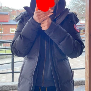 Svart dunjacka från Canada Goose - Säljer en svart dunjacka från Canada Goose med huva och pälskant. Jackan har lång ärm, dragkedja och klassisk patch på ärmen. Perfekt för kalla dagar och riktigt snygg passform. Stilsäker och varm jacka som funkar till allt.