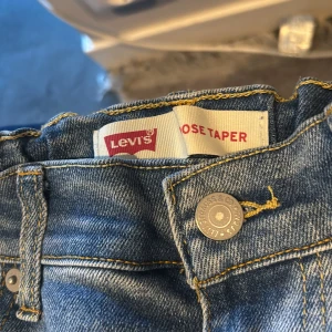Levi's Loose Taper ljusblå jeans - Ljusblå jeans från Levi's i modellen Loose Taper. Klassisk femficksdesign, raka ben med avsmalnande passform och normal midja. Jeansen är tillverkade i denim med snygga kontrastsömmar och metallknapp framtill. Perfekta för en avslappnad och trendig look.