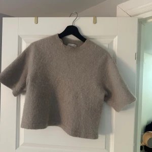 Beige stickad tröja & Other Stories - Superfin beige stickad tröja från & Other Stories. Modellen är croppad med korta ärmar och rund halsringning. Perfekt för lager-på-lager och funkar lika bra till jeans som kjol. Mjuk och skön känsla, enkel att styla till olika looks.