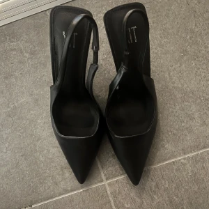 Svarta pumps med spetsig tå - Stilrena svarta pumps från din sko med spetsig tå och öppen häl. Skorna har en smal rem runt hälen och hög klack. Tillverkade i syntetmaterial med en elegant och minimalistisk design som passar perfekt till trendiga looks. Använda endast 1 gång, strl 36 men funkar som 37, då jag själv har 37💕