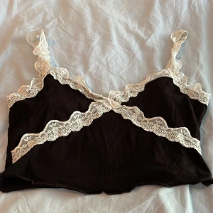 Svart spetslinnetopp från SHEIN - Supersöt svart linnetopp från SHEIN med krämvit spets längs kanterna och axelbanden. Toppen är ärmlös och har en croppad passform, perfekt att styla med jeans eller kjol. Materialet är mjukt och lätt, och spetsdetaljerna ger en romantisk vibe.