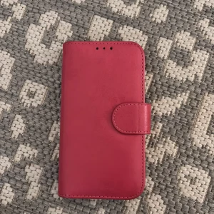 Mörk rosa  plånboksväska till mobil - Snygg mörk rosa plånboksväska till mobil med plats för kort och ID. Väskan har magnetlås och avtagbart mobilskal i svart plast. Stilren design i slätt material, perfekt för att hålla koll på både mobilen och korten.