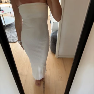 Vit axelbandslös långklänning - Säljer en vit, ribbad långklänning utan axelband. Klänningen har en tight passform med ribbat material. Aldrig använd 