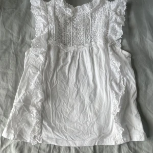 Vit blus - Supersöt vit blus från MNG med broderade spetsvolanger längs axlarna. Små fläckar i armhålorna men de syns inte 