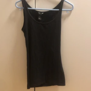 Svart linnetopp från H&M Basic XS - Enkel och stilren svart linnetopp från H&M Basic i storlek XS. Toppen är ärmlös med klassisk rund halsringning och figurnära passform. Perfekt att matcha med jeans eller kjol för en clean look.