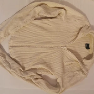 Gul ribbad kofta med dragkedja - Säljer en beige ribbad kofta från Bik Bok i storlek XS. Koftan har lång ärm, är kroppad och hel dragkedja framtill, vilket gör den enkel att ta på och av. Materialet är mjukt och stretchigt, perfekt för lager-på-lager under hösten eller våren.