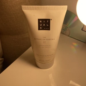 Rituals The Ritual of Sakura body cream - En lyxig body cream från Rituals, The Ritual of Sakura, med doft av rismjölk och körsbärsblom. Tuben är vit med svart och guld logga, innehåller 70 ml. Perfekt för att återfukta huden och ge en fräsch känsla.