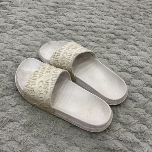 Vita sandaler från newyorker  - Coola vita sandaler från newyorker med präglad text 'VIVA COUTURE' över remmen. Tillverkade i syntetmaterial med platt sula och öppen tå. Perfekta för sommardagar och chill vibes.