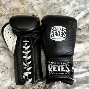Svarta Cleto Reyes boxningshandskar + matchande lindor - Säljer ett par svarta Cleto Reyes boxningshandskar i skinn med klassisk snörning och vit insida. Handskarna kommer med matchande svarta handlindor med broderad logotyp. Perfekta för dig som vill ha proffskänsla på träningen. 14 oz, köpta från jabb.se. Nypris 3100kr