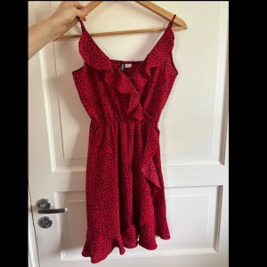 Röd leopardklänning från H&M Divided - Snygg röd kortklänning från H&M Divided med svart leopardmönster. Klänningen har volangdetaljer framtill, smala axelband och markerad midja. Perfekt för dig som vill sticka ut med ett djurmönstrat plagg. Lätt och luftig modell.