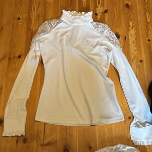 Vit långärmad tävlingstopp - Fin tävlingstopp från horse i storlek 34. Den är långärmad med dragkedja där bak och volanger vid halsen och på slutete av ärmen. toppen har några fläckar på framsidan. Jag tvättar den innan köp med Fläckborttagning eventuellt klorin. om inte fläckarna går bort eller om du köper den utan att jag tvättar den igen så kan du få dem för 15 kr