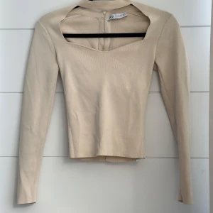 Beige långärmad topp från Zara - Trendig beige långärmad topp från Zara med unik öppen rygg och snyggt skuren halsringning. Toppen är stickad i ett mjukt material och har en slim passform som sitter snyggt på kroppen. .