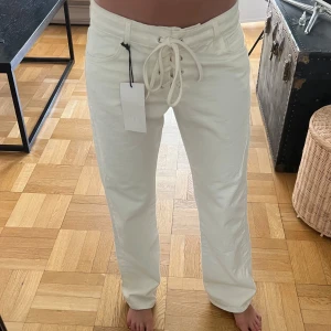 Vita raka byxor med snörning från Zara  - Vita byxor från Zara i rak modell med snygg snörning framtill i midjan. Byxorna har fickor både fram och bak. Jättesnygga och oanvända (jag är 173 cm lång och har oftast 34-36 i jeans) 