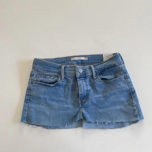 Ljusblå jeanskjol från Levi's - Säljer en ljusblå jeanskjol från Levi's med rå kant nertill och klassiska femficksdetaljer. Modellen är kort , perfekt till sneakers eller boots. Levi's-logga på bakfickan och knappstängning framtill. Superenkel att styla till olika looks.