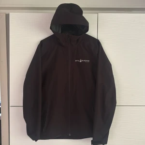 Svart Gore-Tex jacka Sail Racing S - Svart vindjacka från Sail Racing i storlek S, tillverkad i slitstark Gore-Tex. Jackan har huvaoch hel dragkedja framtill.