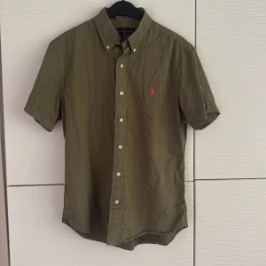 Olivgrön kortärmad skjorta Ralph Lauren - Kortärmad olivgrön skjorta från Ralph Lauren i slim fit. Tillverkad i lätt bomullstwill som känns luftig och skön på sommaren.