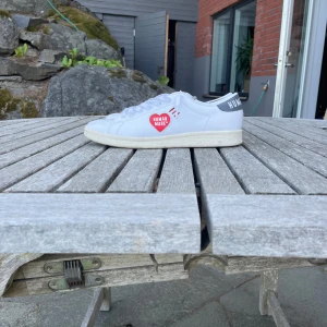 Adidas Stan Smith x Human Made sneakers - Vita Adidas Stan Smith sneakers i samarbete med Human Made. Skorna har klassisk låg siluett, snörning och detaljer i grått på hälen med texten 'HUMAN MADE' och 'DRY ALLS'. Röd Human Made-logga på sidan. Tillverkade i skinn med platt sula och rund tå. Väldigt bra skick och riktig snygga och unika 😊