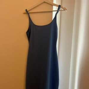 Blå stilren klänning - En stilren ljus blä långklänning med smala axelband och enkel, rak passform. Klänningen är ärmlös och har en mjuk, något stretchig känsla som gör den bekväm att bära. Aldrig använd och slutar precis under knäna.