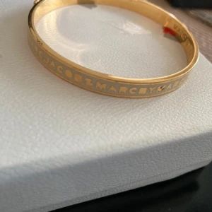 Guldigt armband Marc by Marc Jacobs - Snyggt armband i guldton från Marc by Marc Jacobs med ingraverad logga runt hela. 