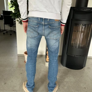 Replay anbass ljusblå slim jeans - Snygga ljusblå jeans från Replay med klassisk femficksdesign och läderpatch bak. Jeansen har en slim passform, raka ben och är tillverkade i mjukt denimtyg. Perfekta för dig som gillar en stilren och modern look.