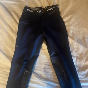 Marinblå ridleggings från CRW - Marinblå ridleggings från CRW med bred resår med logga. Snygga detaljer med grepp på insidan av benen för extra fäste i sadeln. Stretchigt syntetmaterial som sitter tight och bekvämt. 
